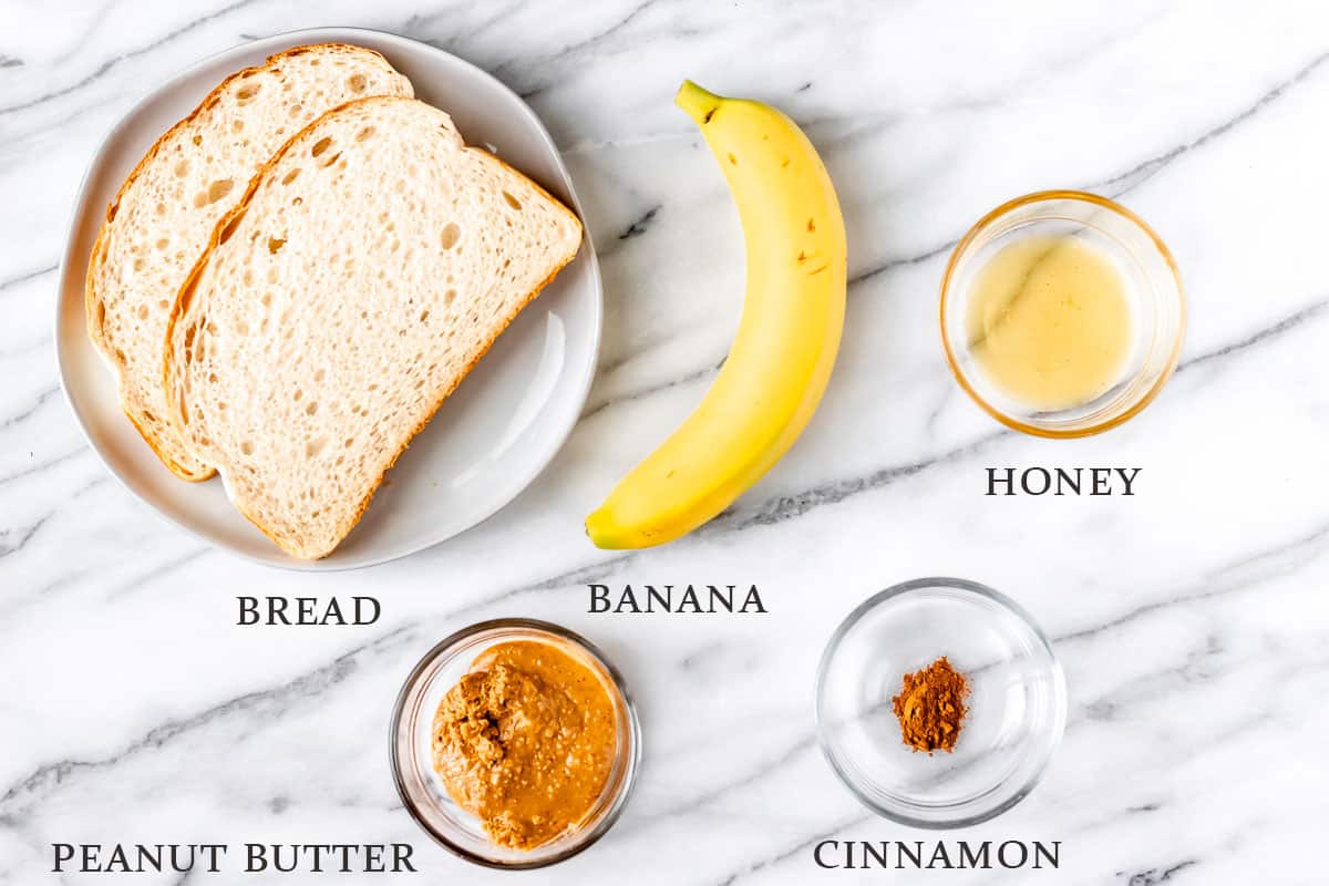 Ingredients to make a fried peanut butter and panini sandwich on a marble background with text overlay.