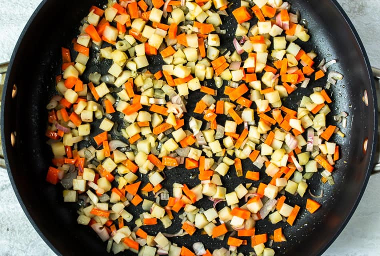 Carrots, shallots, and water chestnuts cooking in a black skillet