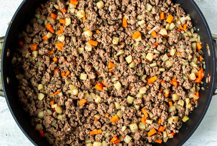 Ground beef, carrots, shallot, and water chestnuts cooking in a black skillet