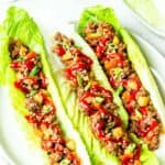 3 Ground Beef Lettuce Wraps on a white plate over a white background with extra lettuce on a white plate and a white cup in the background