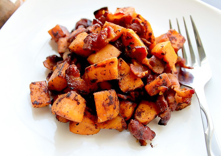Sweet potato and bacon hash on a white plate with a fork