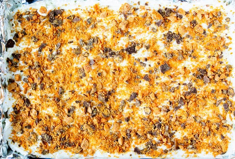 Butterfinger candy on top of cheesecake in a rectangular pan