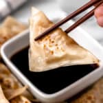 A potsticker being lifted up over a bowl of dipping sauce with chopsticks.