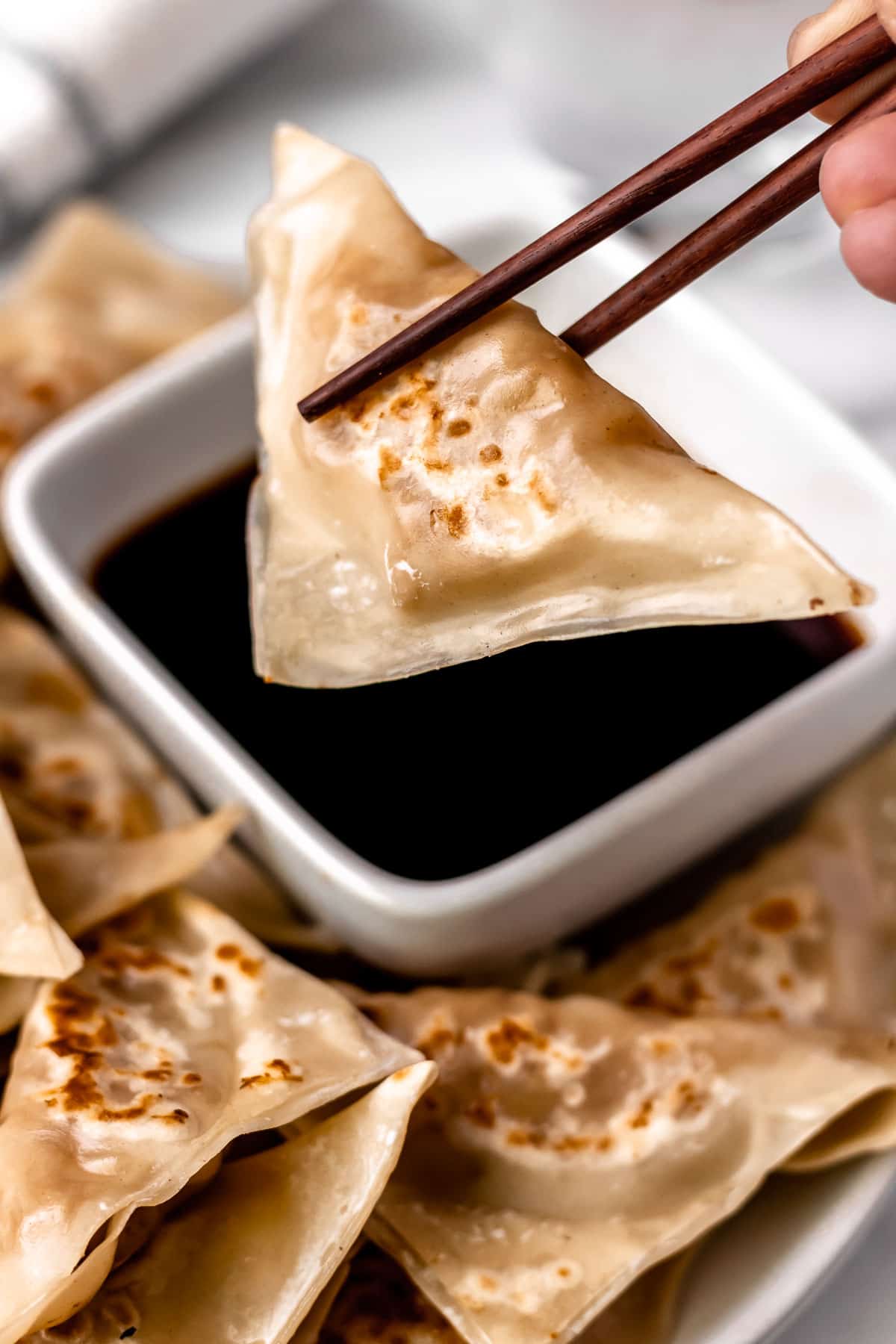 A potsticker being lifted up over a bowl of dipping sauce with chopsticks.