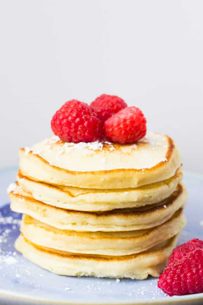 A Stack Of Lemon Ricotta Pancakes with Raspberries on Top on a blue plate with a white background