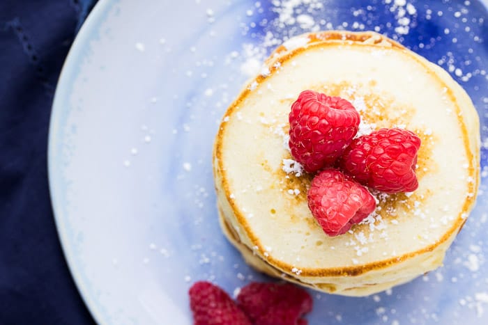 Overhead Of Pancakes on a Blue Plate with Raspberries and powdered sugar on Top and off to the side