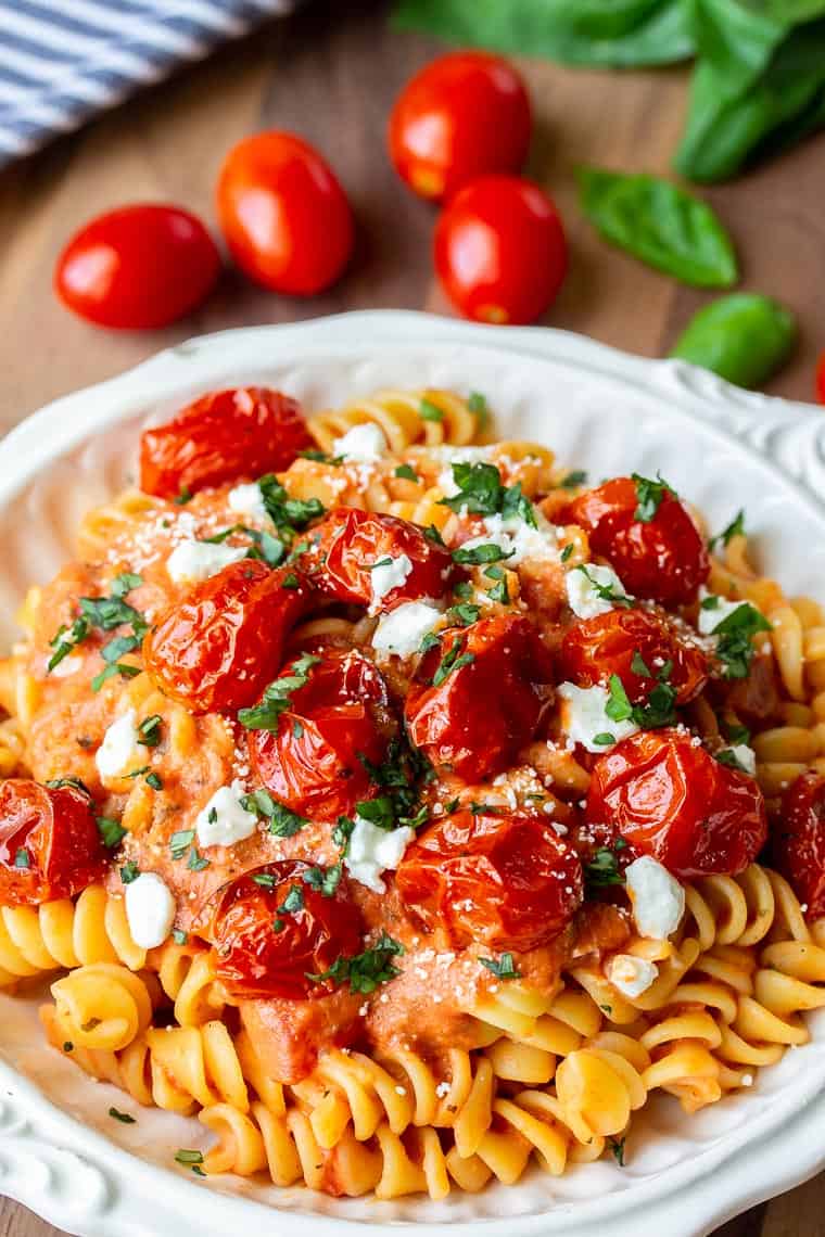 Close up of Goat Cheese Pasta Sauce over Rotini Pasta with cherry tomatoes and fresh basil in the background over a wood board