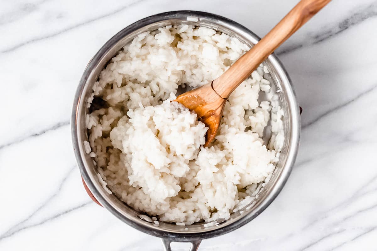 Cooked rice in a silver pot with a wood spoon