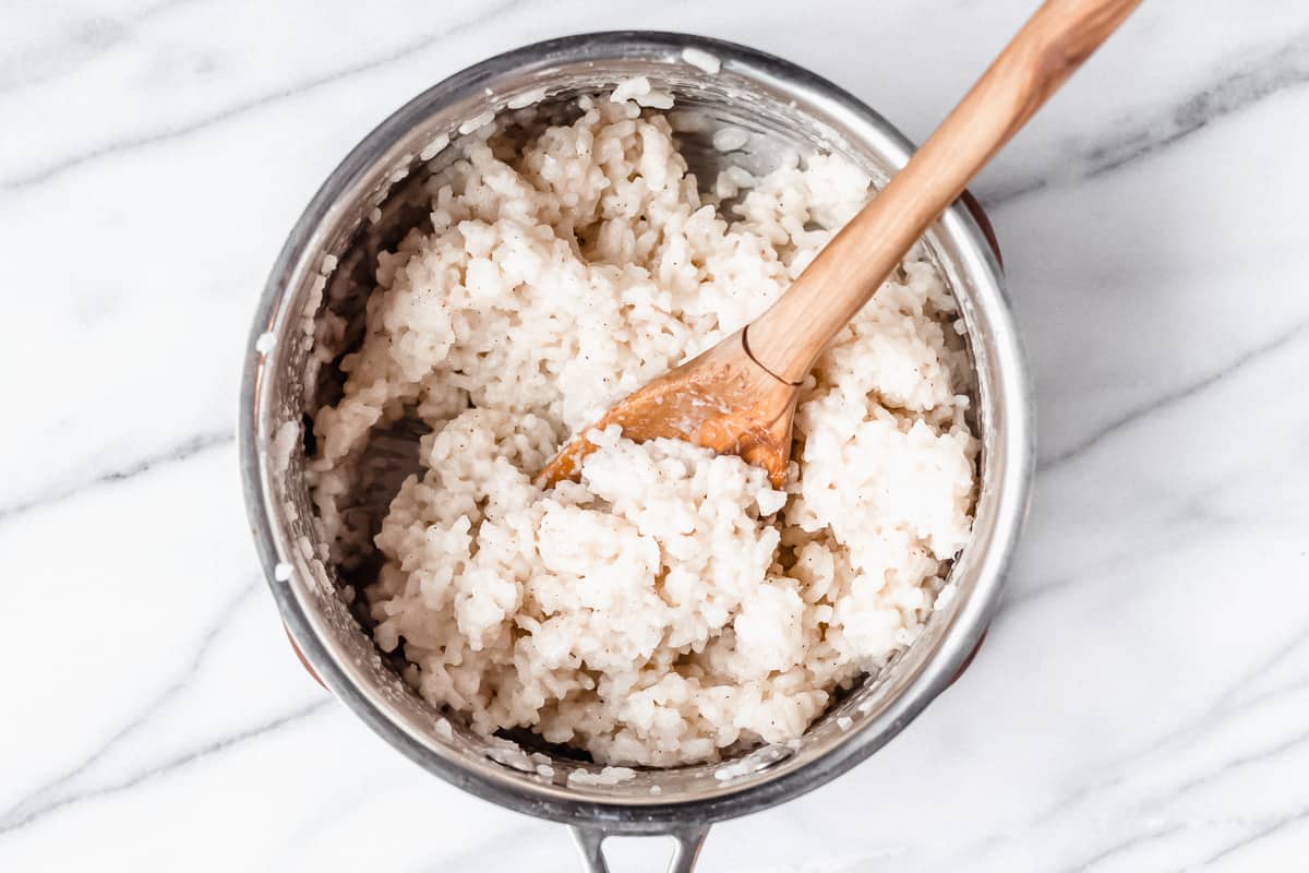 White rice with brown sugar, nutmeg and cream mixed into it in a silver pot with a wood spoon