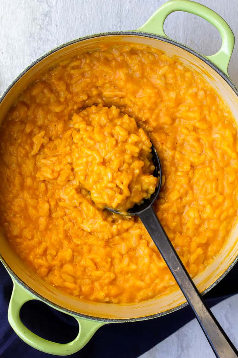 Pumpkin Risotto in a dutch oven with a black spoon scooping some up