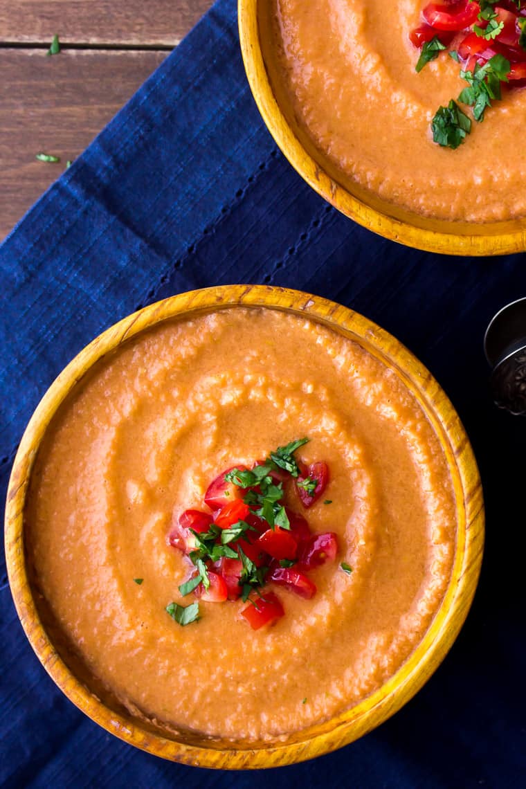 Overhead view of 2 orange bowls filled with blender gazpacho soup on a blue napkin and wood background