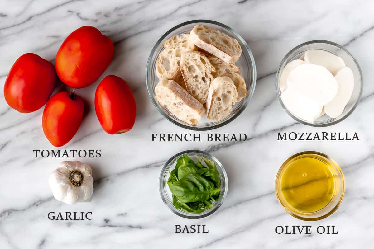 Ingredients to make bruschetta on a marble background with text overlay.