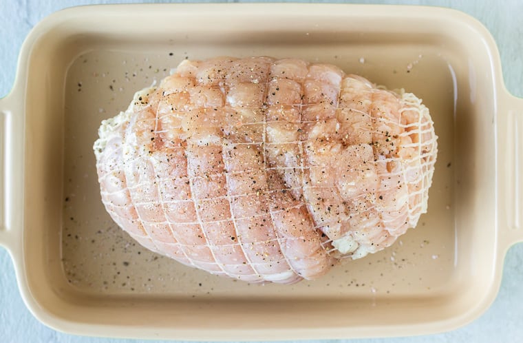 A raw turkey breast in a baking dish seasoned with salt and pepper