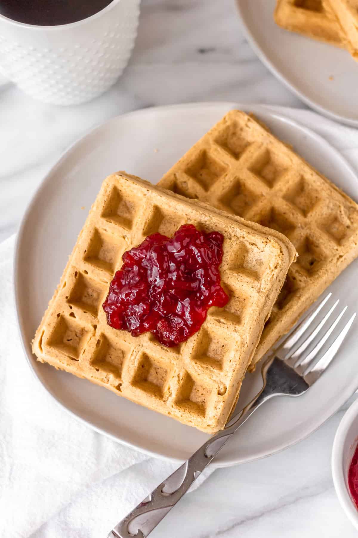 CLose up of two gluten free peanut butter waffles on a plate with a fork.