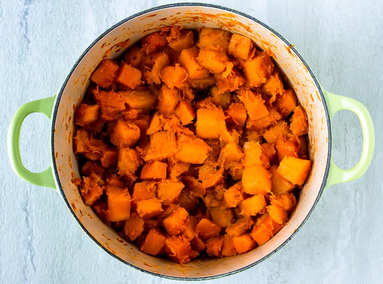 Cooked cubes of butternut squash in a Dutch oven over a white background