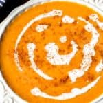 Close up of savory butternut squash soup in a white bowl over a wood board with a spoon and blue and white towel partially showing in the background