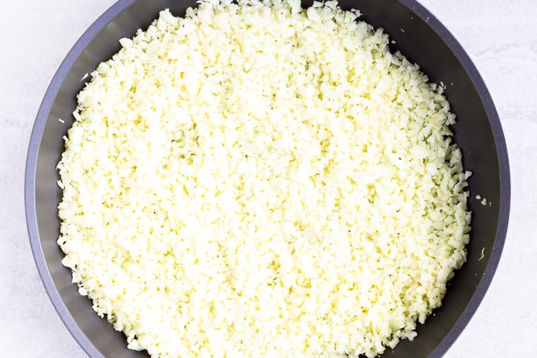 Rice cauliflower cooking in a black skillet over a white background