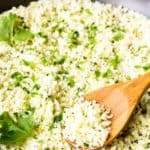 close up of cilantro lime cauliflower rice in a black skillet with a wood spoon