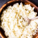 Creamy Coconut Cauliflower Rice in a wood bowl with a fork in it over a gray background