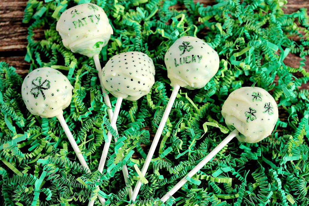 St. Patrick's Day inspired Green Cake Pops laying on green easter grass on a wood board