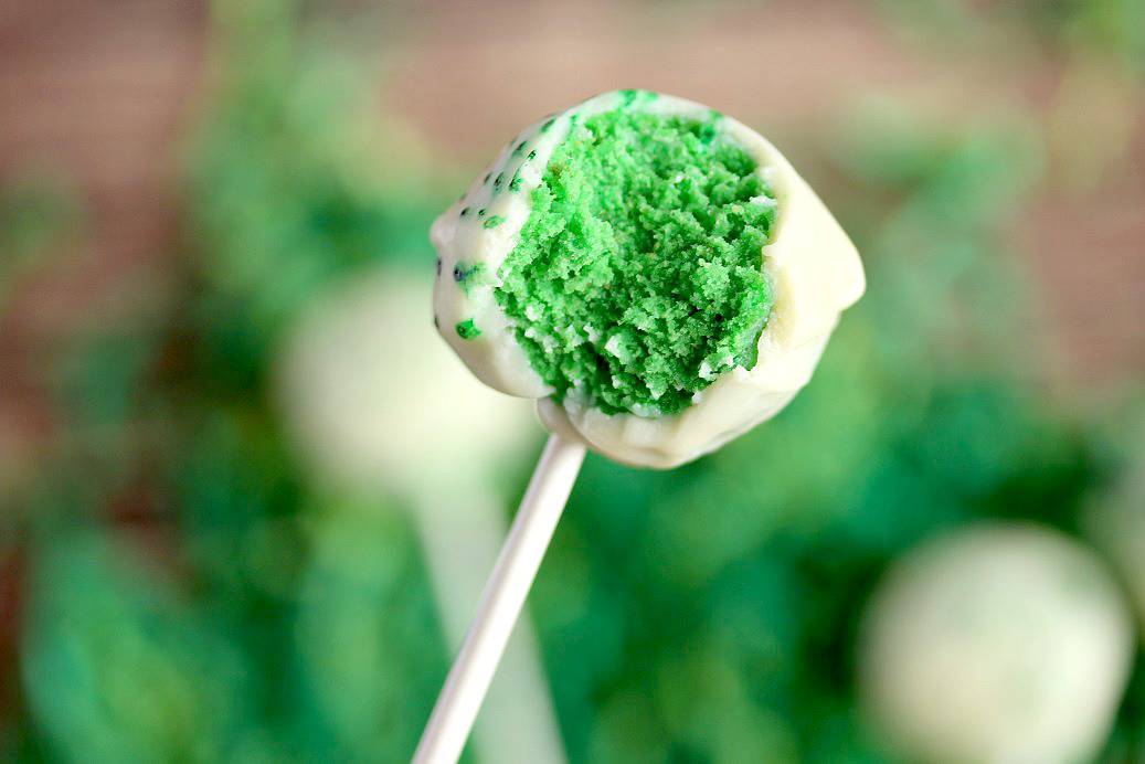 close up Inside View of a green cake pop with white chocolate coating with more blurred in the background