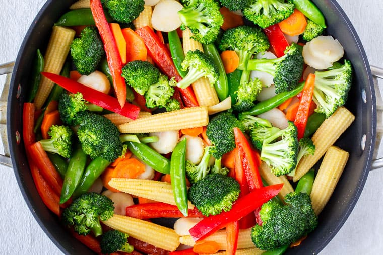 A combination of stir fry vegetables cooking in a deep, black skillet