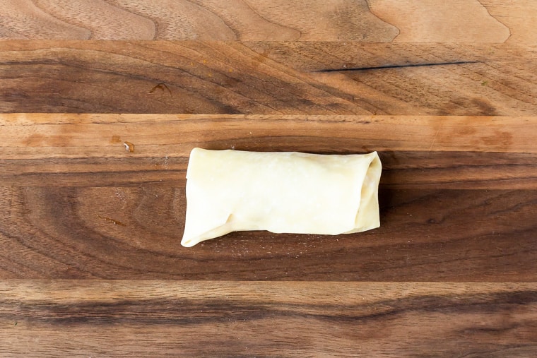 A completely folded up egg roll on a wood board