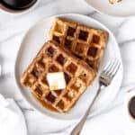 Overhead of peanut butter and chocolate swirled waffles on a plate with a second plate partially showing and a cup of coffee.