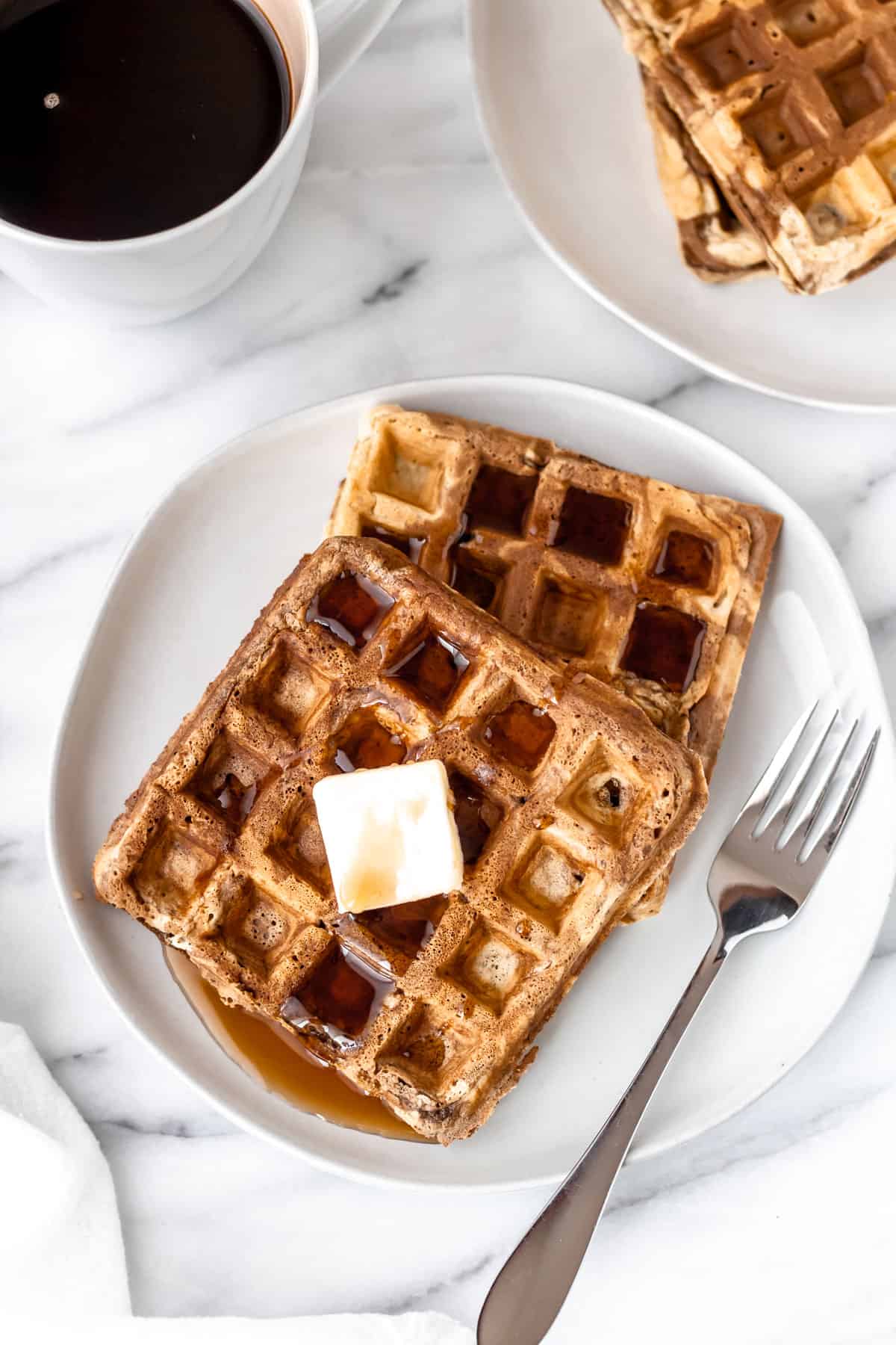Overhead of peanut butter and chocolate swirled waffles on a plate with a second plate partially showing and a cup of coffee.