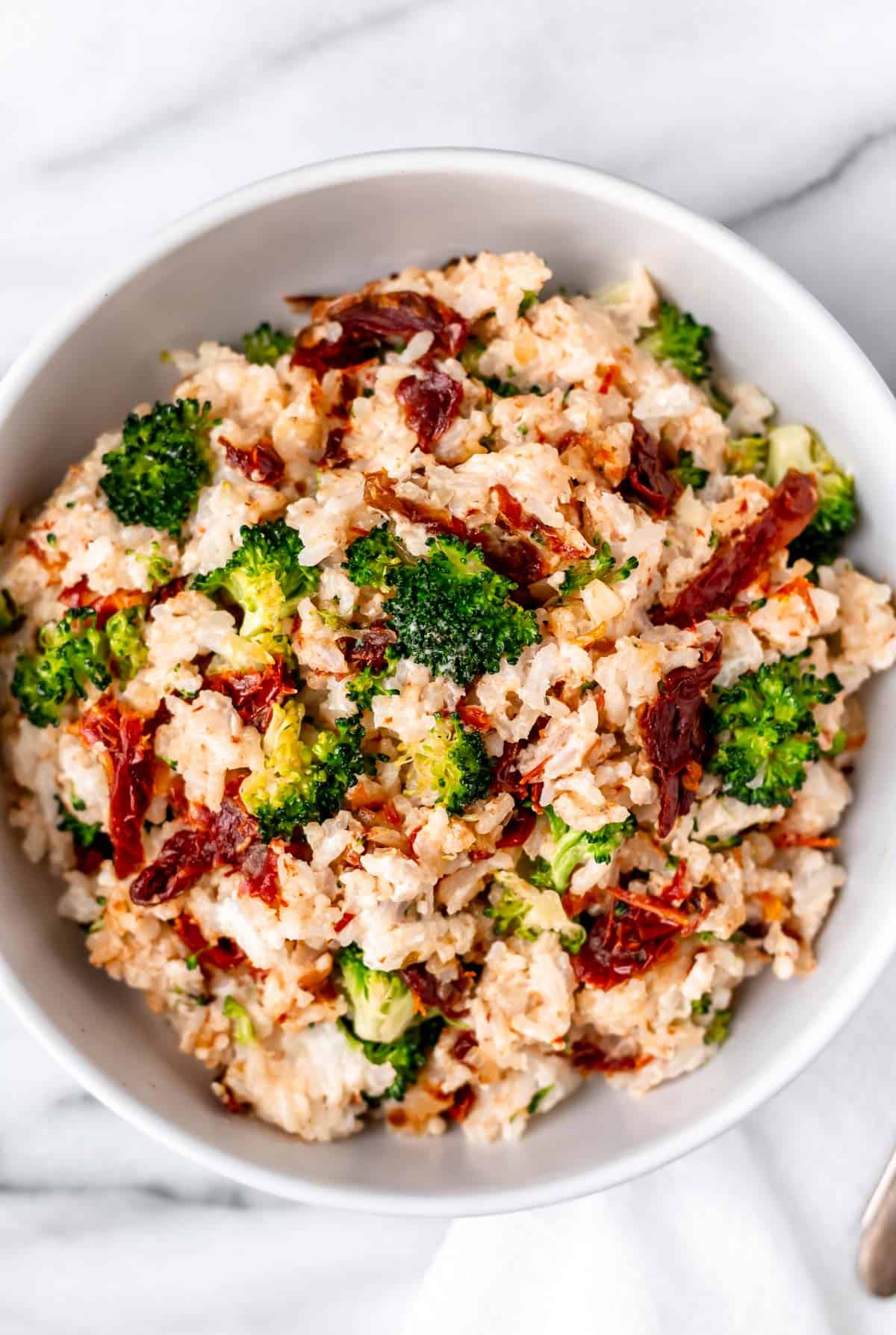 Overhead of a bowl of cream cheese rice with broccoli and sun-dried tomatoes.