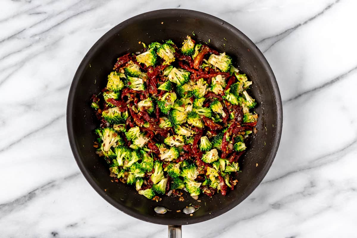 Sun-dried tomatoes and broccoli cooking in a skillet.