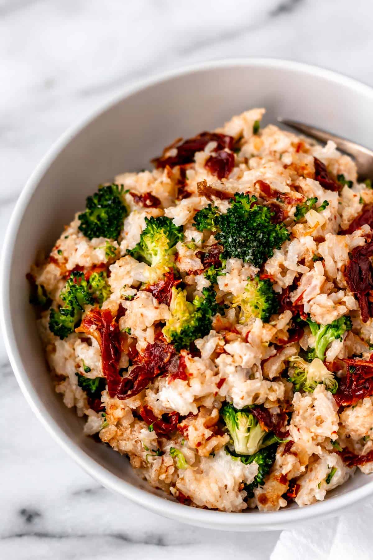 A bowl of cream cheese rice with broccoli and sun-dried tomatoes close up.