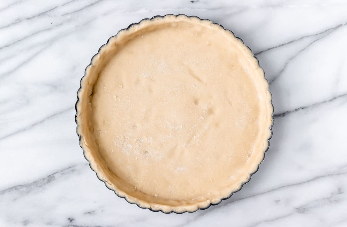 A tart pan filled with tart dough on a marble table.