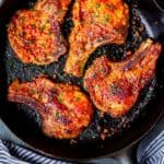 4 Orange Chipotle Pork Chops in a cast iron skillet over a gray background with a blue and white striped towel at the bottom