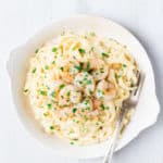A white bowl with Creamy Garlic Parmesan Shrimp Pasta and a fork over a white background