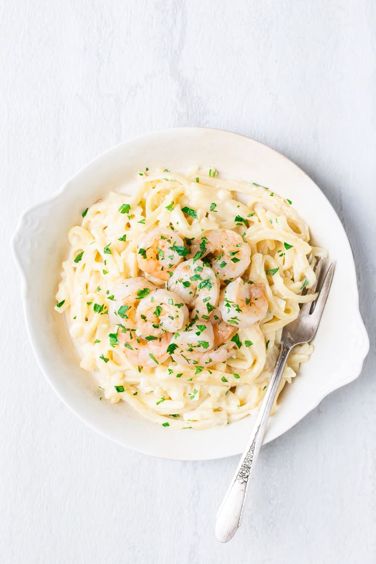 A white bowl with Creamy Garlic Parmesan Shrimp Pasta and a fork over a white background