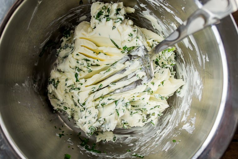 Herbs and cream cheese being masked together with a fork in a silver bowl