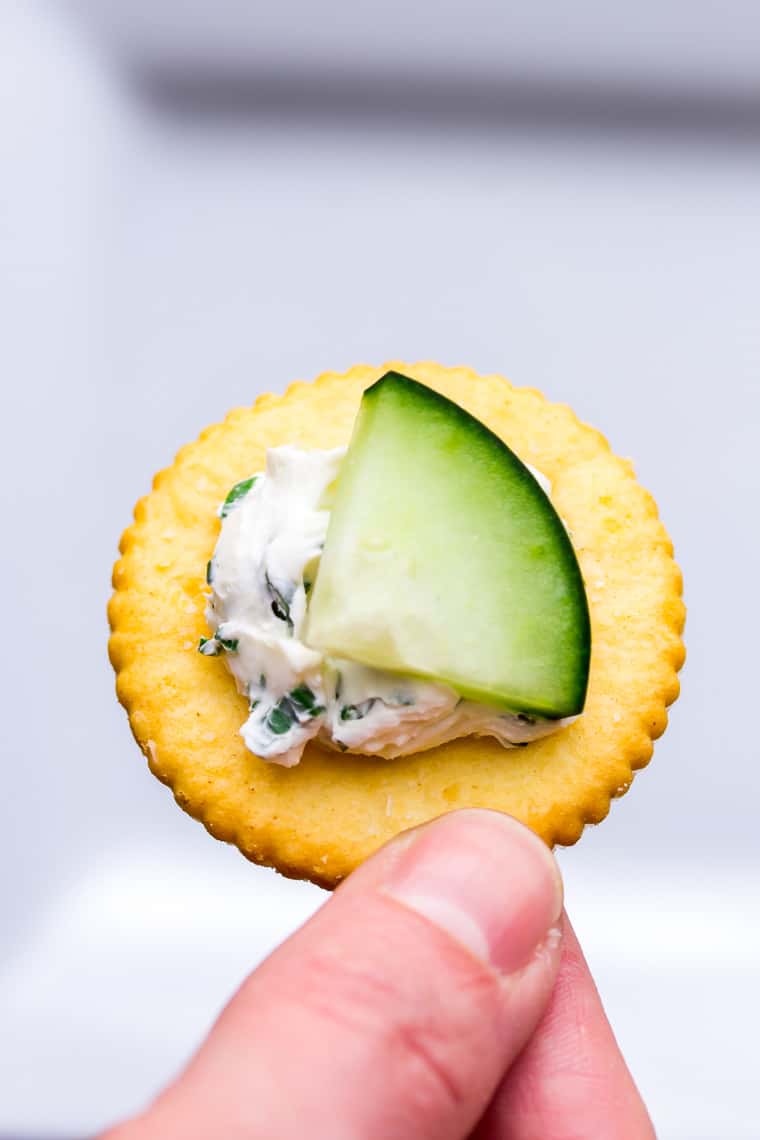 A single Herbed Cream Cheese Cucumber Cracker being held up over a white background