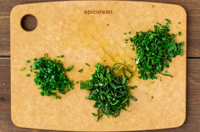 Chives, parsley, and basil finely chopped on a wood cutting board