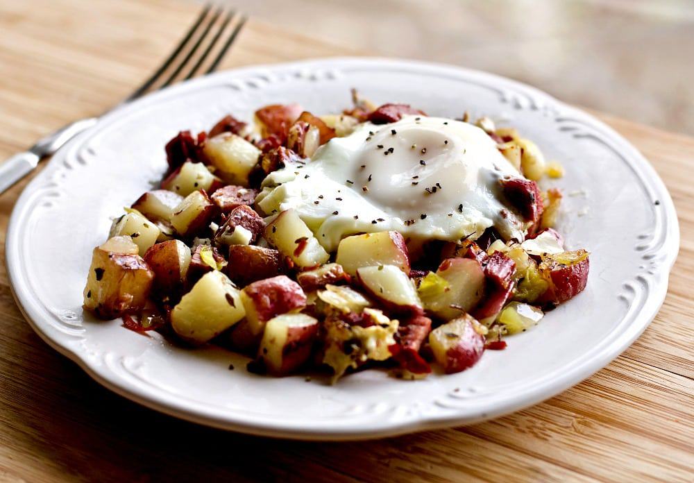 Corned Beef Hash and Eggs on a white plate on a wood table with a fork in the background