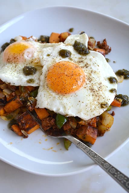 Chorizo and Sweet Potato Breakfast Hash Topped with 2 Eggs on a White Plate on a White Background