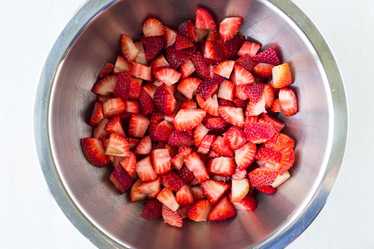 Cut strawberries in a silver bowl over a white background