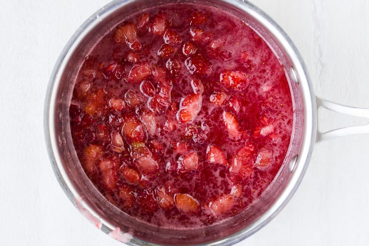 Strawberry puree in a silver saucepan over a white background