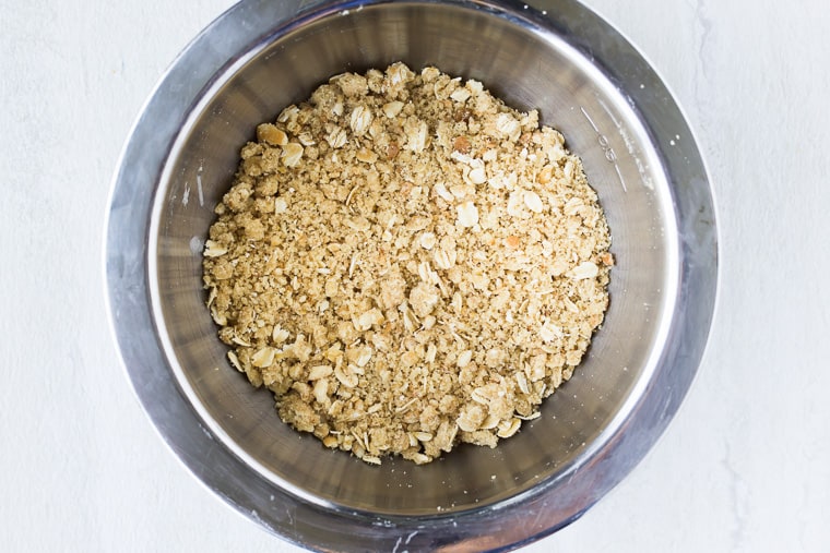 Oat crumble in a silver bowl over a white background
