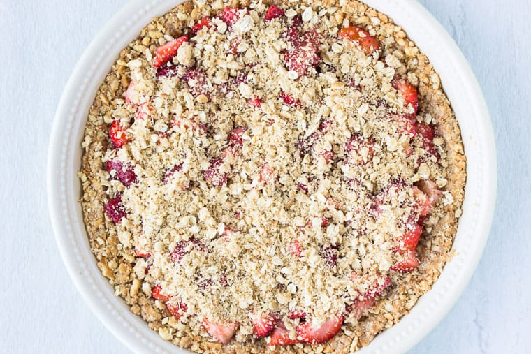 strawberry pie with crumb topping before baking in a pie pan over a white background