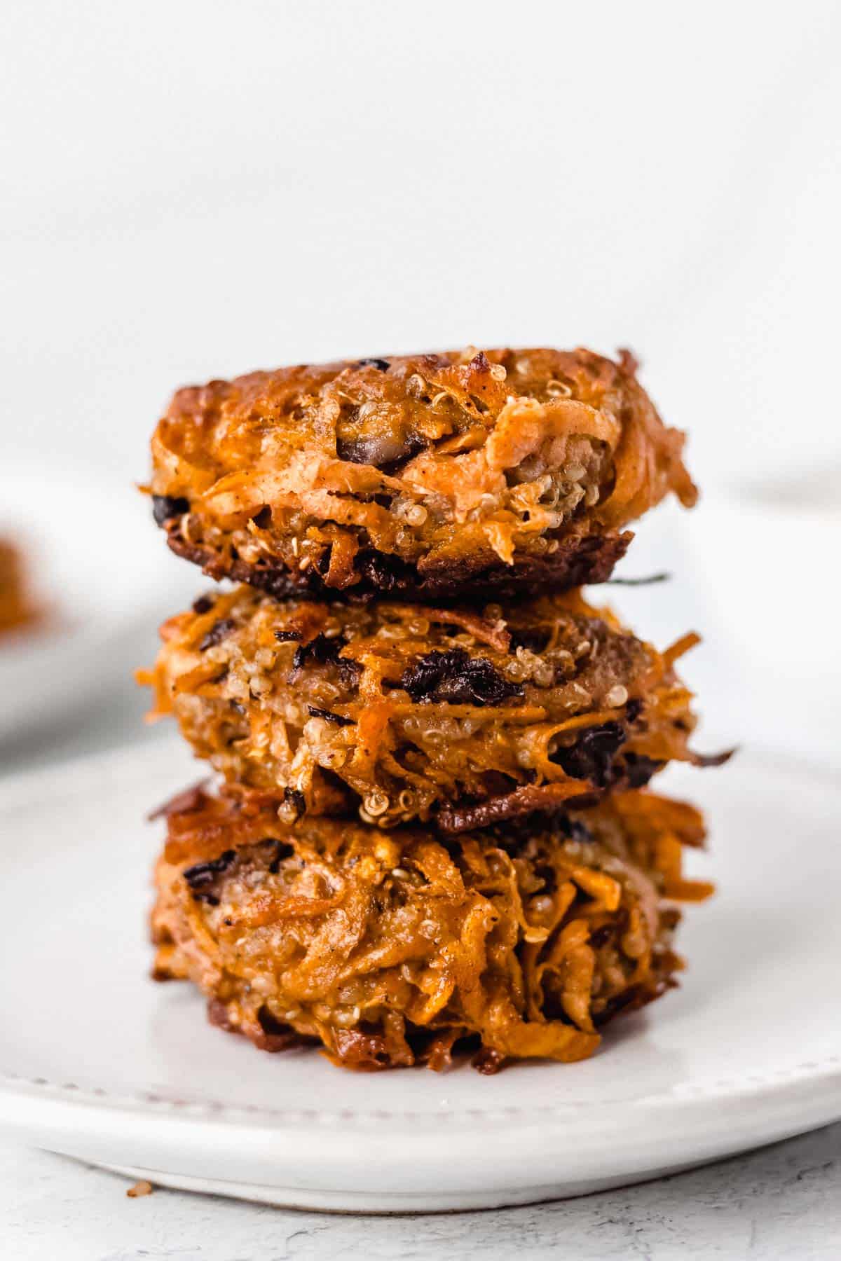 3 sweet potato fritters stacked on top of each other on a white plate over a white background