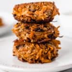 3 sweet potato fritters stacked on top of each other on a white plate over a white background