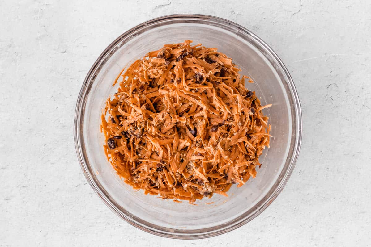 Shredded sweet potato, black beans, quinoa and spices in a clear bowl over a white background