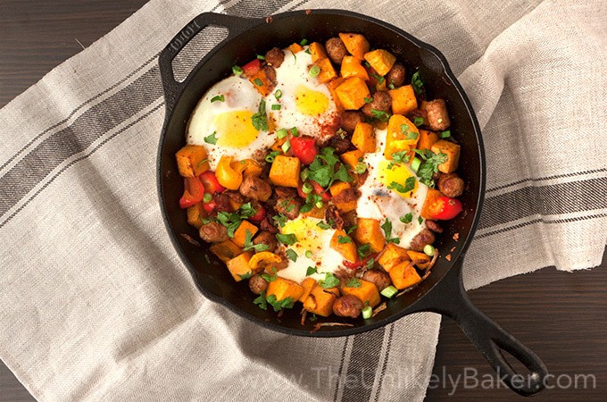 Sweet Potato Breakfast Hash with Sausage, Bacon, and Egg in a black skillet with a gray and black towel on a gray background