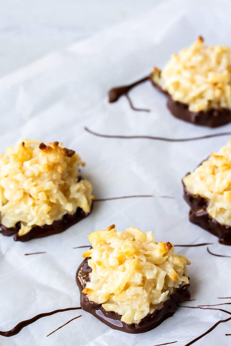Close up of a chocolate dipped coconut macaroon on parchment paper with 3 more macaroons in the background